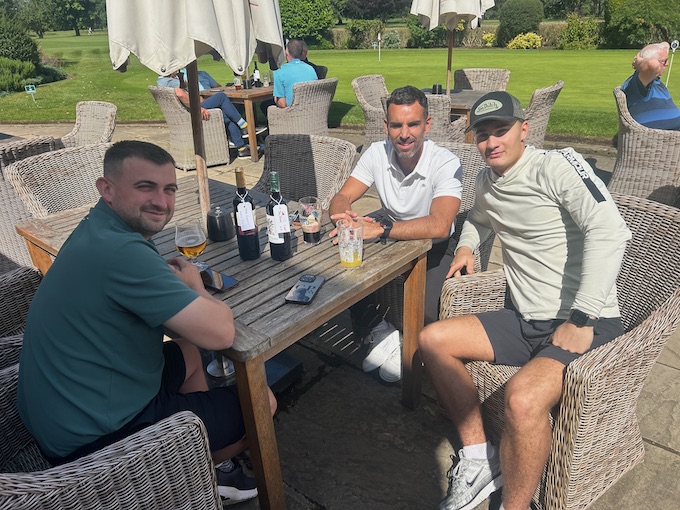 Three members at a terrace table with the course behind